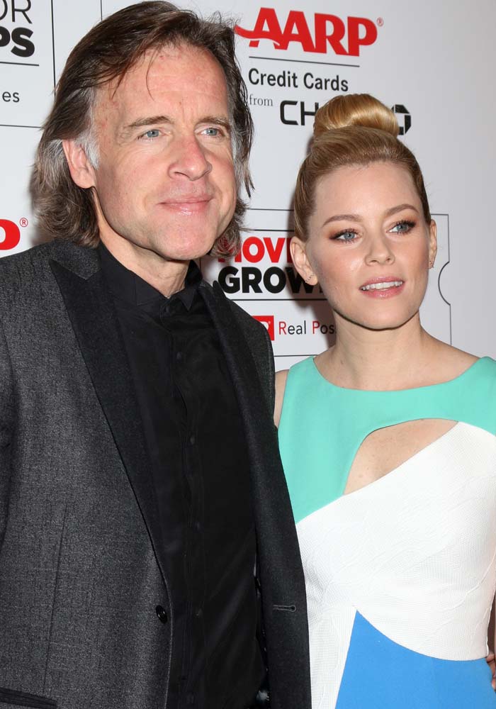 Elizabeth Banks poses alongside director Bill Pohlad on the red carpet, pairing her modern cutout dress with a minimalist clutch and bold orange heels for a cohesive finish