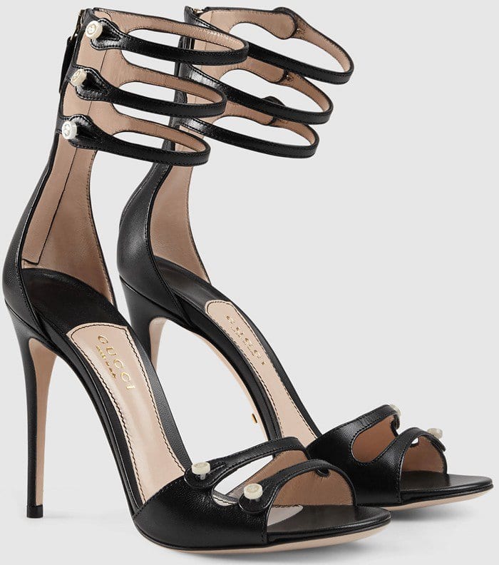 Gucci's black patent button-strap sandals combine a sleek open-toe silhouette with pearl-accented ankle straps, reflecting Alessandro Michele's talent for turning classic evening footwear into something quietly eccentric