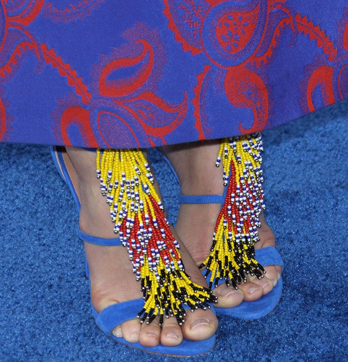 The fringe sways across her toes in layered strands of yellow, red, black, and white beads, creating a kinetic focal point