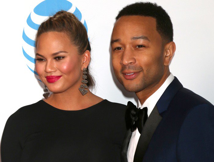 Chrissy Teigen and John Legend pose together at the NAACP Image Awards, with Teigen complementing her sleek black gown with bold statement earrings and classic red lipstick