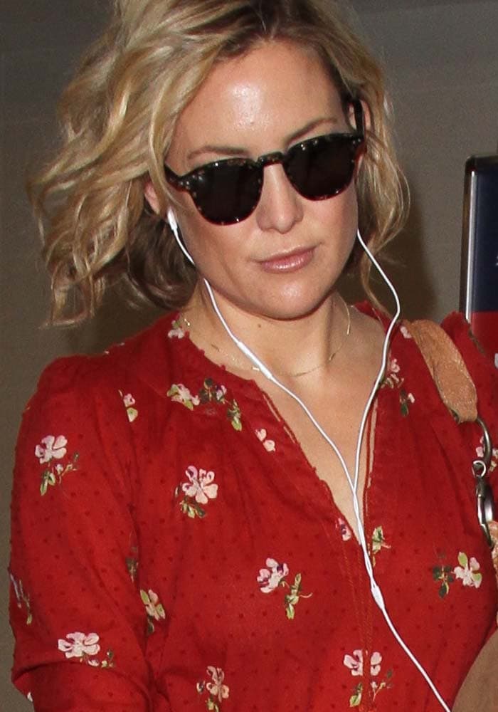 Kate Hudson keeps her airport look relaxed and bohemian in a red floral midi dress, tousled waves, oversized sunglasses, and white earphones while heading through LAX