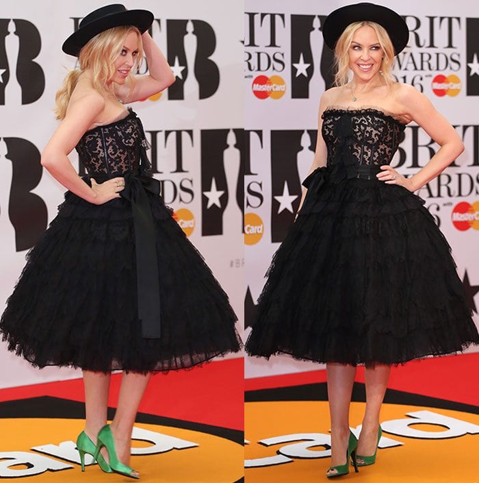 Kylie Minogue stuns in a playful black lace Dolce Gabbana dress, paired with bold emerald green satin pumps and a wide-brimmed hat at the 2016 BRIT Awards