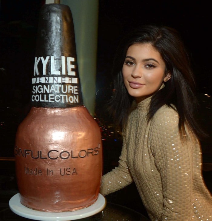 Kylie Jenner leans beside an oversized nail polish bottle display celebrating her Signature SinfulColors collection