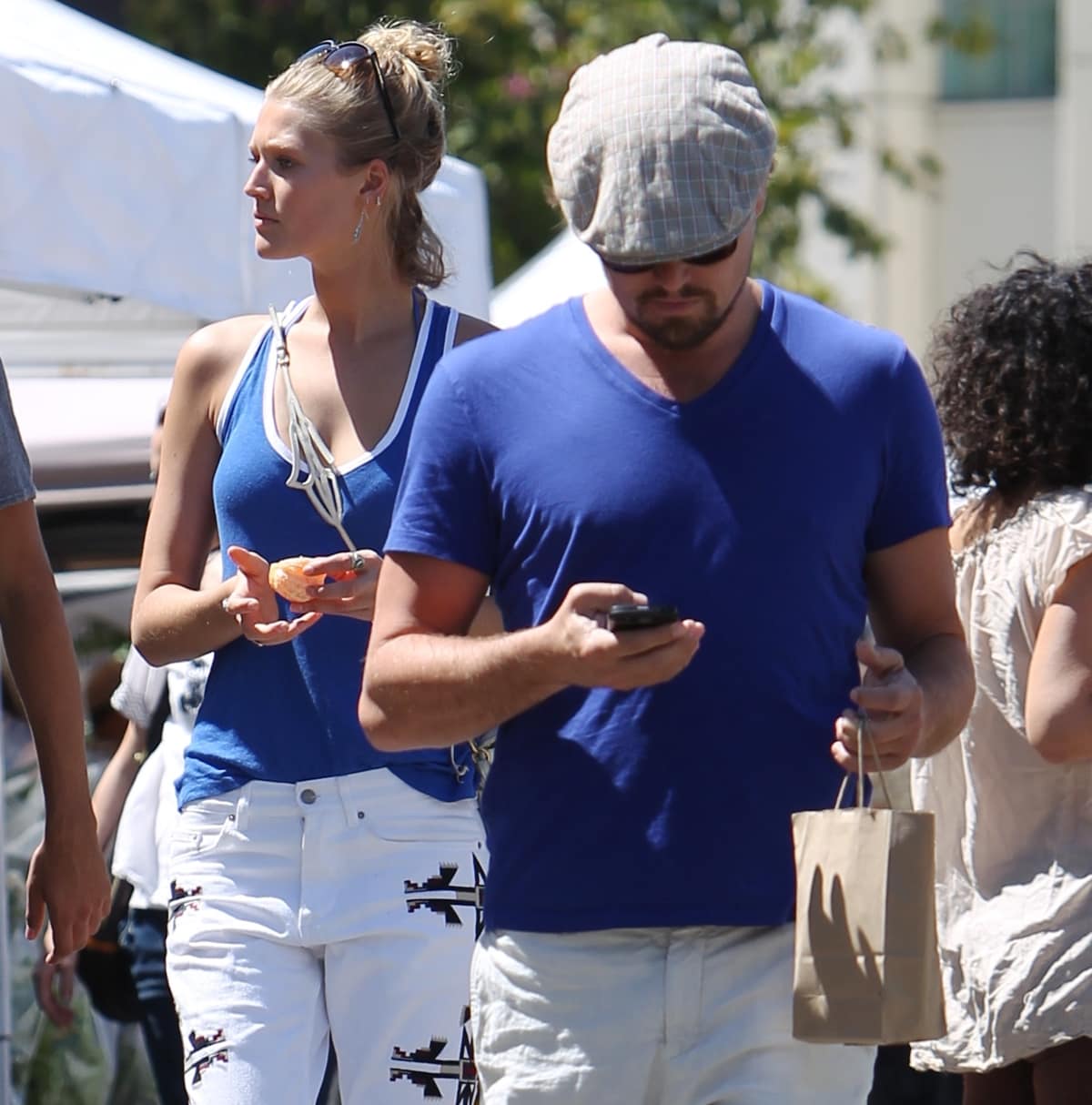 Toni Garrn, in a cobalt blue tank top and white printed jeans, towers over Leonardo DiCaprio, who kept it casual in a blue tee, white shorts, and a flat cap