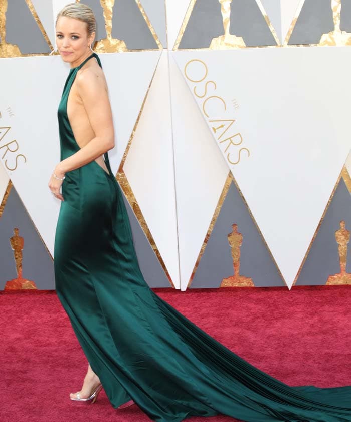 A dramatic side view reveals the gown’s fluid drape and open-back silhouette as it trails elegantly across the carpet