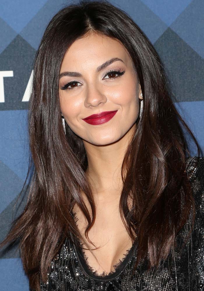 Victoria Justice showcases a glamorous look with her dark brown hair styled sleek and straight, perfectly complementing her bold red lipstick and defined eye makeup that highlights her brown eyes