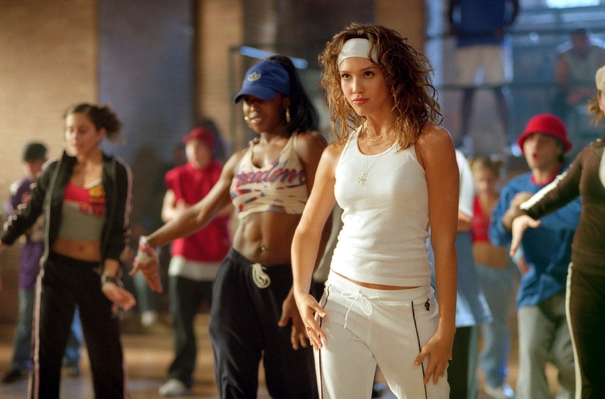 Jessica Alba channels early-2000s streetwear as Honey Daniels, sporting a white tank, matching track pants, and a signature headband in a dance rehearsal scene from Honey (2003)