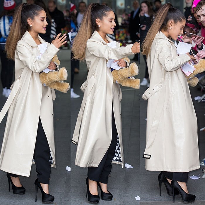 Ariana Grande greets fans outside BBC Radio 1 studios in London, layering a sleek Dawn Levy trench coat over a daring Self-Portrait jumpsuit and finishing the look with towering black Giuseppe Zanotti platform pumps