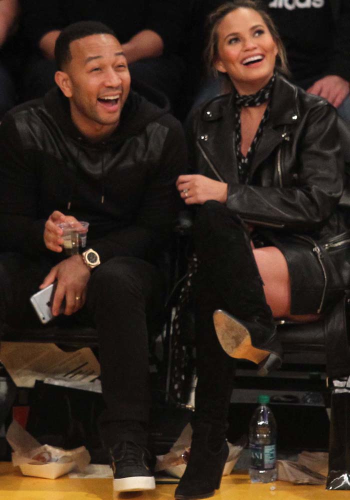 John Legend and Chrissy Teigen coordinate in sleek black outfits while sitting courtside at a Los Angeles Lakers game