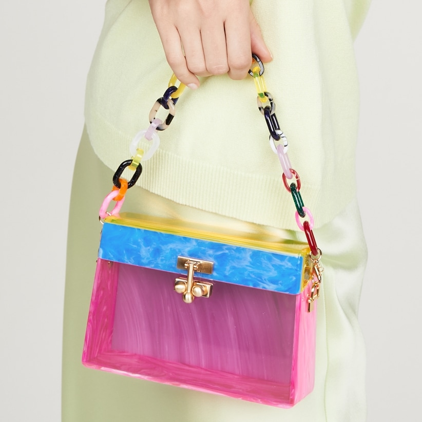 The Edie Parker Miss Mini clutch pairs translucent pink acrylic with marbled blue and yellow panels, a colorful resin-link handle, and polished gold hardware for a playful take on the brand's signature box bag