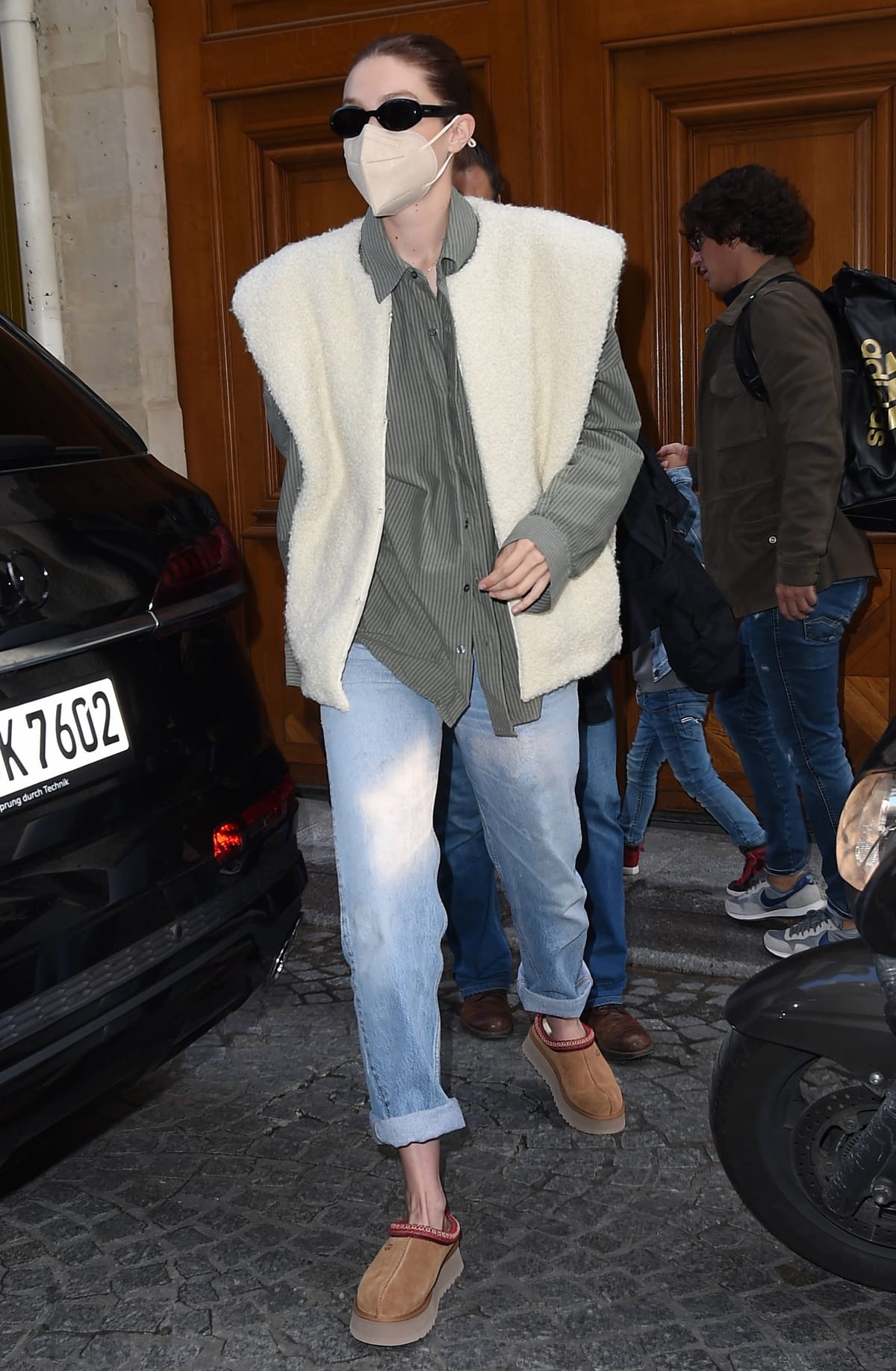 Gigi Hadid steps out in Paris wearing UGG Tazz platform slippers with cuffed jeans, a striped button-down, and an oversized Isabel Marant shearling vest on September 29, 2021, blending fashion-week practicality with the relaxed styling that helped make the cozy mule a street-style staple