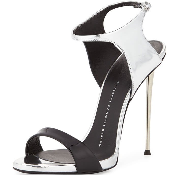 Giuseppe Zanotti's patent-and-metallic ankle-wrap sandals combine metallic silver calfskin, glossy black patent leather toe bands, slim ankle-wrap straps, and approximately 4.5-inch (11.5 cm) metal pin heels, creating a striking two-tone design that retailed for $1,195 when introduced in 2016