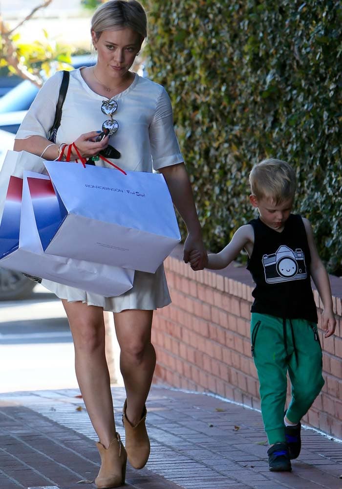 Walking hand in hand with Luca after a shopping trip, Duff balanced practicality and style in a breezy dress paired with tan ankle boots