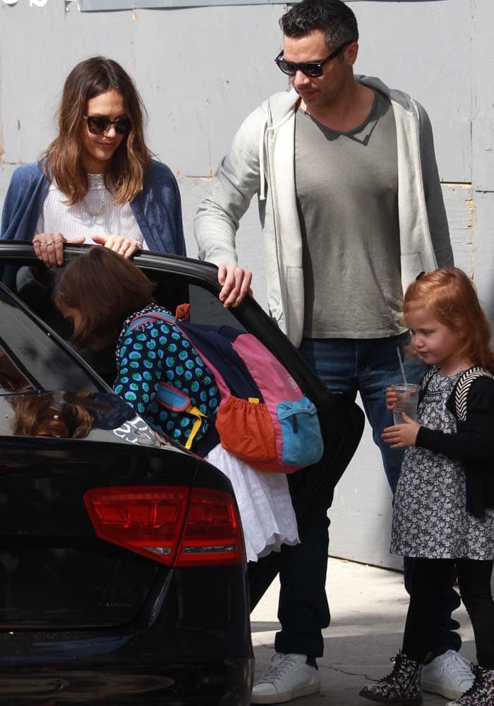 Jessica Alba and her husband Cash Warren help their daughters into the car during a casual family outing, with the actress keeping her look relaxed in sunglasses and a light cardigan