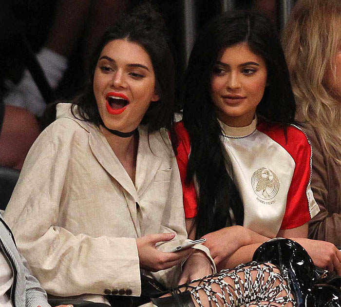 Kendall Jenner shares a lively courtside moment at the Lakers game, her vibrant orange-red lipstick adding a playful pop to her chic oversized blazer look