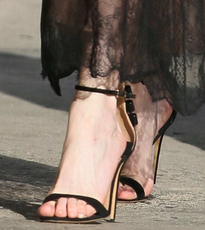 Kirsten Dunst steps out in Salvatore Ferragamo “Angie” sandals, showcasing sleek black ankle straps, a minimalist open toe, and delicate bow accents that frame her feet atop slender, leg-lengthening stiletto heels