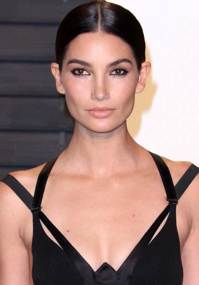 Lily Aldridge sharpens the look with a sleek center-parted updo and sculpted, neutral-toned makeup, letting the architectural lines of her outfit take full focus