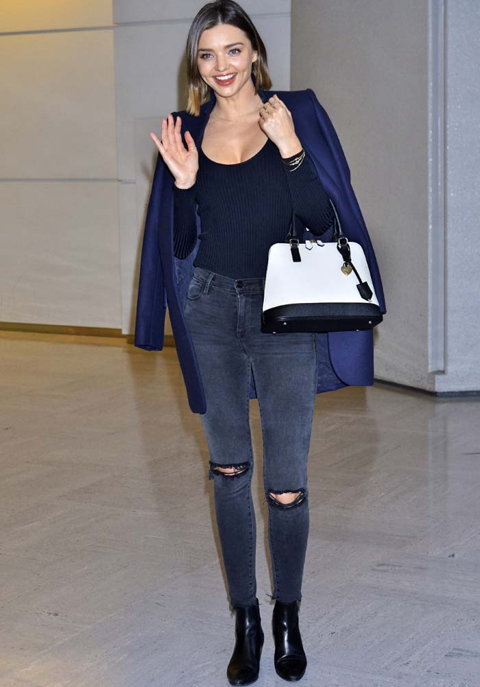 Miranda Kerr paired sleek Saint Laurent ankle boots with distressed J Brand skinny jeans, a fitted ribbed top, and a tailored Stella McCartney coat, creating a polished travel look that balanced comfort, practicality, and understated sophistication