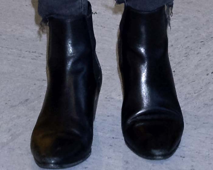 Close-up of Miranda Kerr's black Saint Laurent ankle boots, showcasing the sleek leather finish, rounded almond toes, and low block heels that made them a practical yet polished choice for airport travel