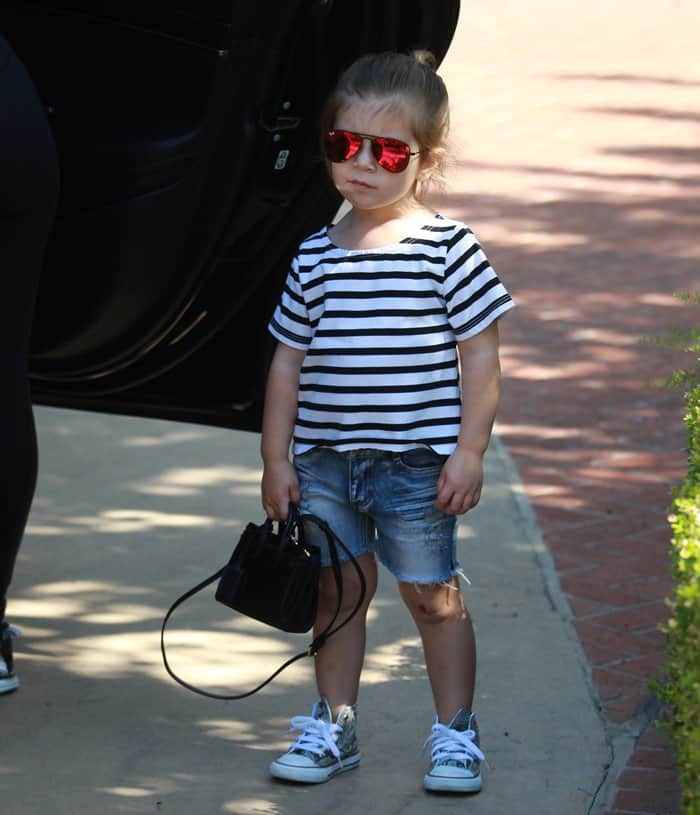 Penelope Disick exudes mini fashionista vibes outside her Hollywood Hills home on February 26, 2016, rocking a striped tee, distressed denim shorts, silver high-top sneakers, red mirrored sunglasses, and a chic black mini handbag
