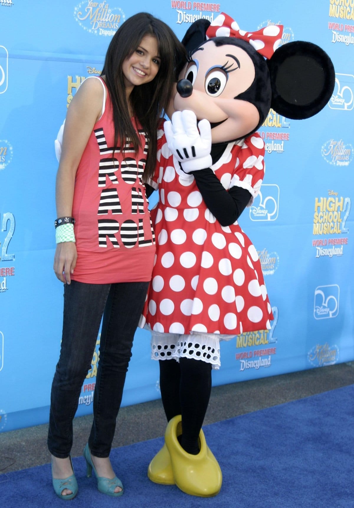 At the High School Musical 2 world premiere at Disneyland in August 2007, a teenage Selena Gomez embraced playful early-2000s style in a pink “Let Rock ’n’ Roll” tank, skinny jeans, and teal peep-toe pumps — a look that hinted at the confident fashion evolution to come
