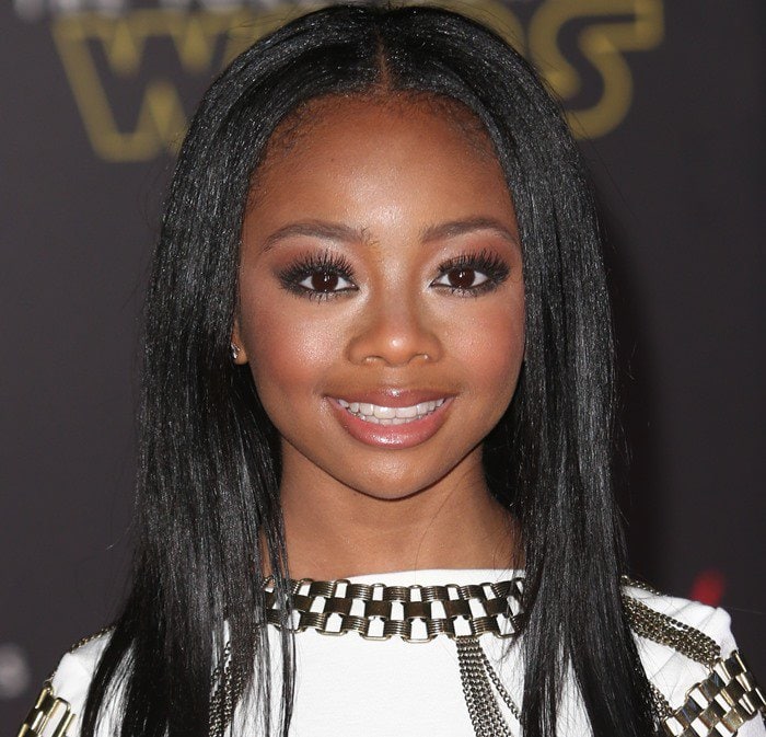 Skai Jackson wears her hair sleek and straight with a center part, perfectly framing her face and highlighting her warm brown eyes, which complement her glowing makeup look