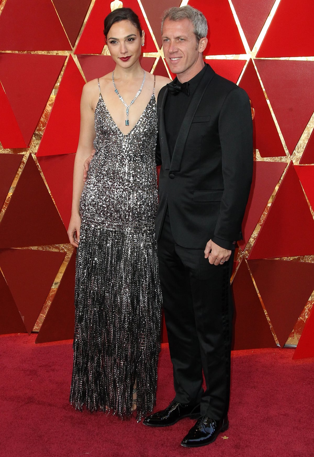 Gal Gadot wears a Givenchy dress and stunning Tiffany Co. diamond necklace on the red carpet with her husband Yaron Varsano at the 2018 Academy Awards