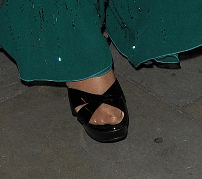 Mariah Carey completes her St. Patrick’s Day look with black patent sandals featuring cross-toe straps and a platform heel, paired with sheer nylons