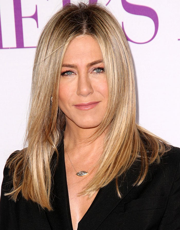 Jennifer Aniston keeps her look classic with sleek, straight hair and a delicate gold pendant necklace featuring an evil eye charm