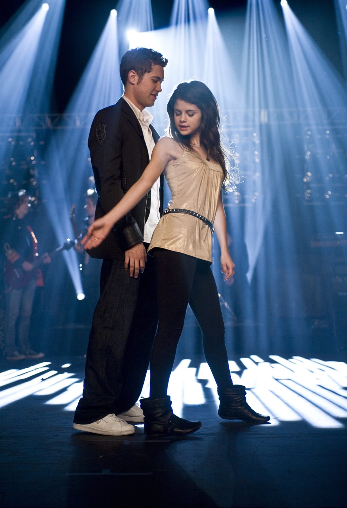 Selena Gomez channels modern-day Cinderella energy in sleek black leggings, a gold camisole top, and ankle-high leather dance boots while performing opposite Drew Seeley, who pairs his black blazer with crisp white sneakers