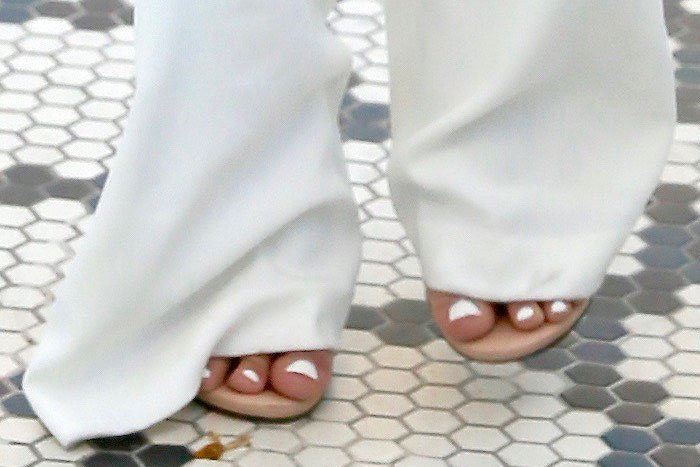 A close-up reveals Ariel Winter’s nude open-toe sandals peeking out beneath her flared white trousers, paired with a crisp white pedicure