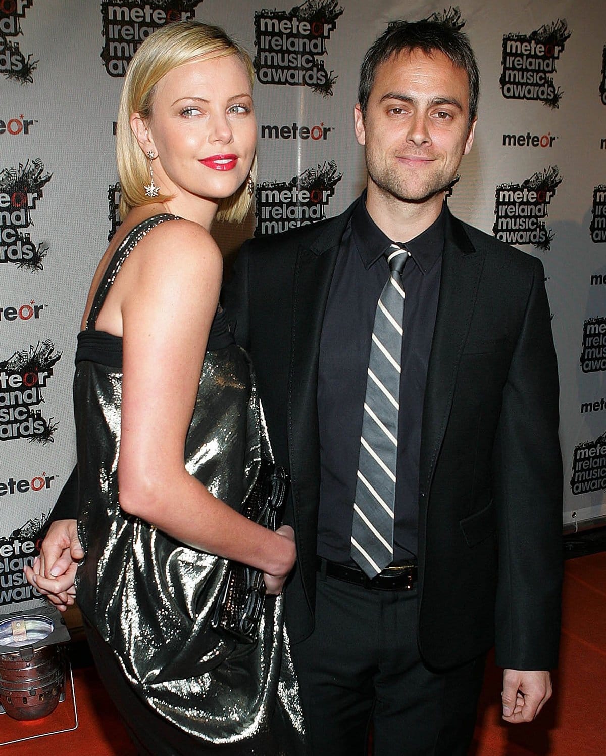 Charlize Theron shines in a metallic one-shoulder dress with a matching oversized clutch at the Meteor Ireland Music Awards, posing alongside then-boyfriend Stuart Townsend