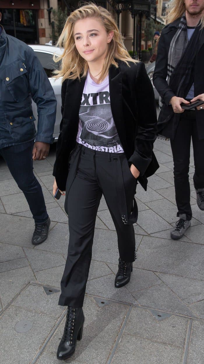 Chloë Grace Moretz looks effortlessly stylish with her loose, wavy hair, natural makeup, and a bold graphic t-shirt paired with chic pants and a sleek black jacket
