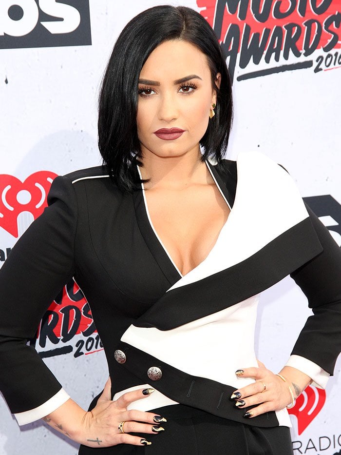 Demi Lovato shows off her wrist and hand tattoos while posing in an Alexander McQueen jacket