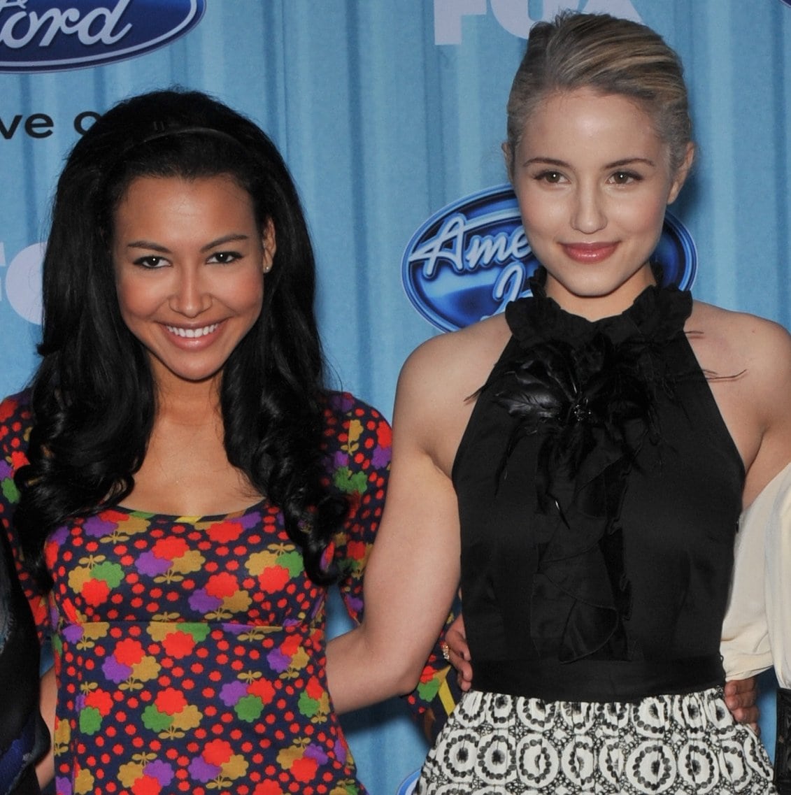 Naya Rivera stands beside her Glee co-star Dianna Agron, wearing a playful multicolored floral-print dress, while Agron opts for a chic black halter top with ruffled detailing and a patterned skirt at an American Idol event