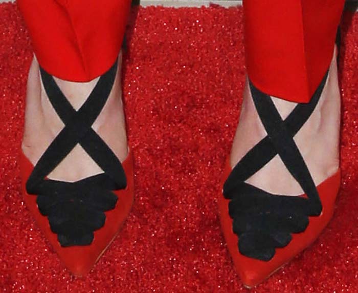 Emilia Clarke finishes the look with unreleased Kurt Geiger pumps, where black crisscross straps and scalloped detailing sharpen the pointed toe and add graphic contrast against the bold red suit