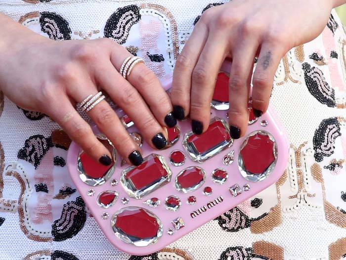 Emilia Clarke grips a jewel-embellished Miu Miu clutch, its oversized crystals and glossy pink finish adding a playful, high-shine contrast to her graphic dress