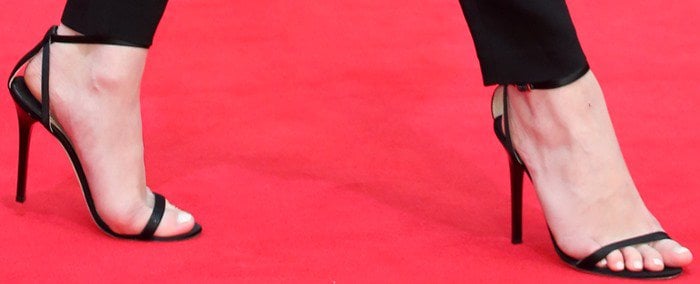 A close-up highlights Emily VanCamp’s sleek black leather Jimmy Choo “Minny” sandals, whose delicate ankle straps and razor-thin stilettos add a refined, elongating finish to her red-carpet look