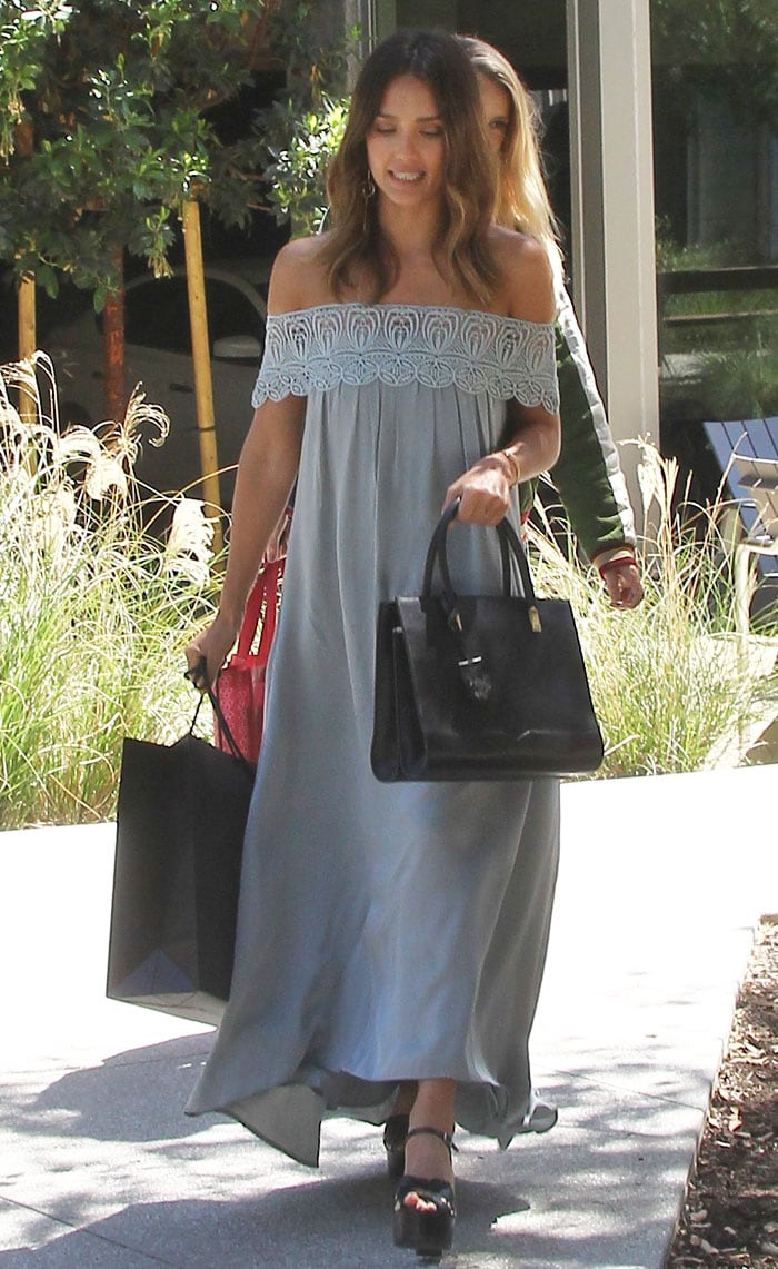 The flowing silhouette of Alba’s pale gray bardot dress contrasts with the bold height of her black Saint Laurent “Candy” sandals