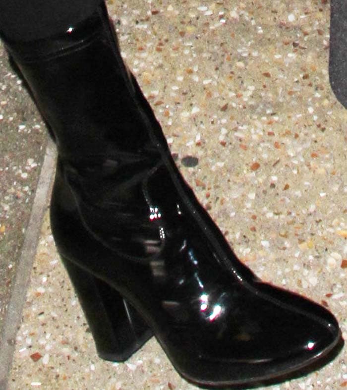 A closer look at her footwear reveals sleek black patent ankle boots with a squared toe and sturdy block heel, balancing height with walkable stability