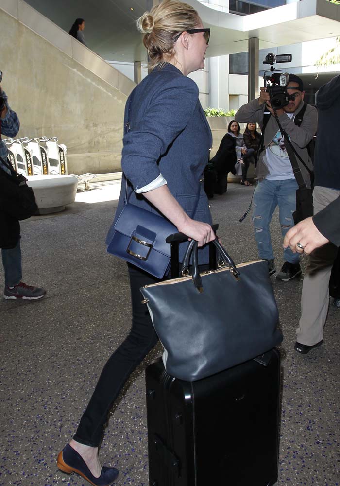 A structured Ferragamo top-handle bag and crossbody add a refined, ladylike contrast to her relaxed airport uniform