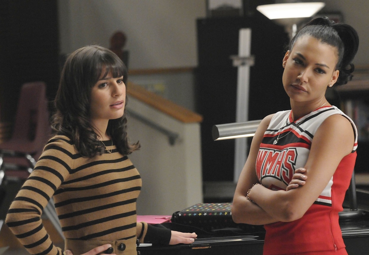 Lea Michele as Rachel Berry wears a retro-inspired camel and black striped sweater dress, while Naya Rivera as Santana Lopez sports the iconic WMHS cheerleading uniform in this classic scene from Glee