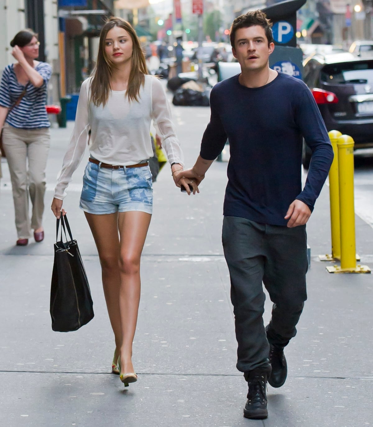 Miranda Kerr keeps it chic in printed denim shorts, a sheer white blouse, and lime green pumps, while Orlando Bloom opts for a casual navy long-sleeve and rugged boots