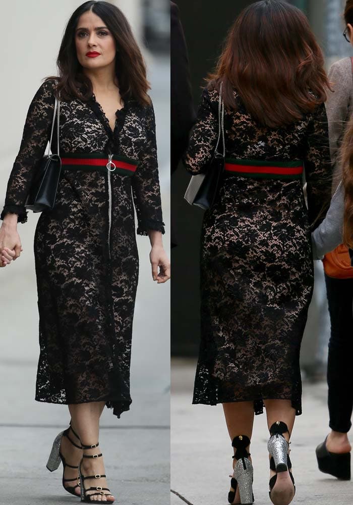 Salma Hayek steps out in a sheer black lace Gucci dress cinched with the brand’s signature striped belt, pairing the bold look with glitter-covered Giambattista Valli block heels and strappy front detailing