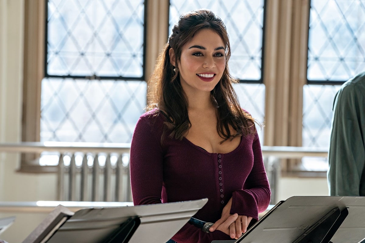 In a scene from "Tick, Tick... Boom!," Vanessa Hudgens, as Karessa Johnson, performs in a ribbed, deep burgundy top with a scoop neckline and button details, paired with delicate drop earrings
