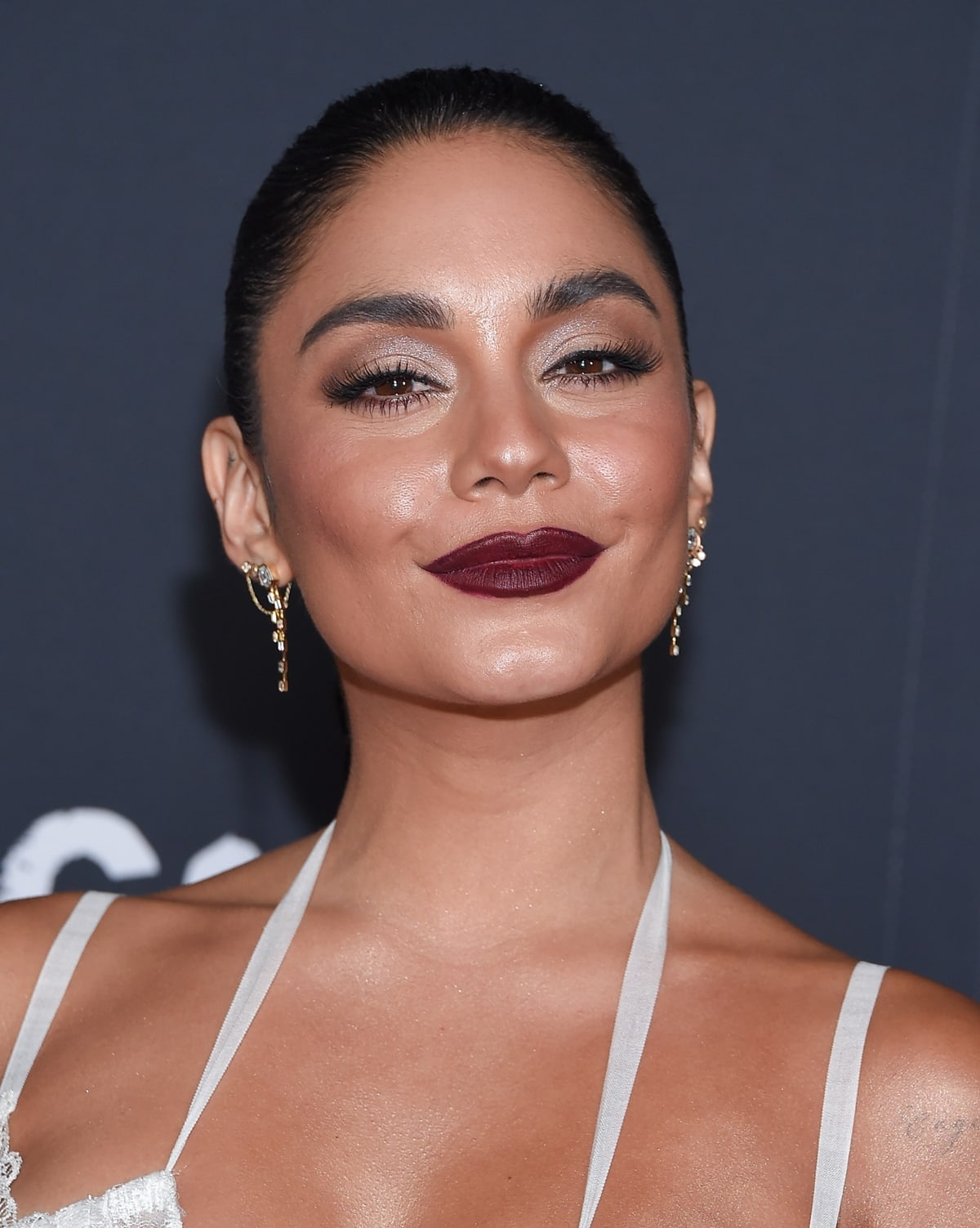 Vanessa Hudgens' red carpet look is defined by a bold and dramatic makeup choice, featuring a deep, rich berry-hued lip and a shimmering, smokey eye with defined lashes