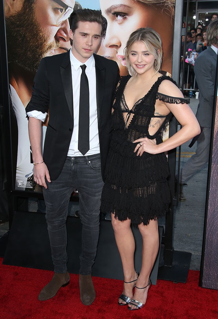 Chloë Grace Moretz and Brooklyn Beckham coordinate in monochrome looks, with her lacy black Alexander McQueen dress perfectly complementing his slim-cut suit and suede boots