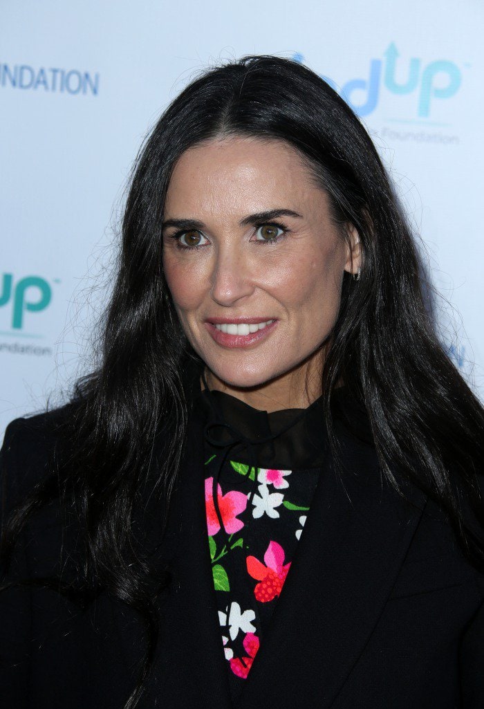 Demi Moore showcases her signature long waves and fresh, natural glam, which complement the vibrant floral print peeking through her black coat