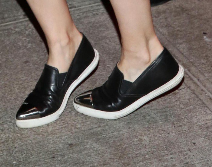 Her black leather Miu Miu slip-on sneakers feature sleek metallic cap toes and white rubber soles, balancing comfort with a sharp, modern finish