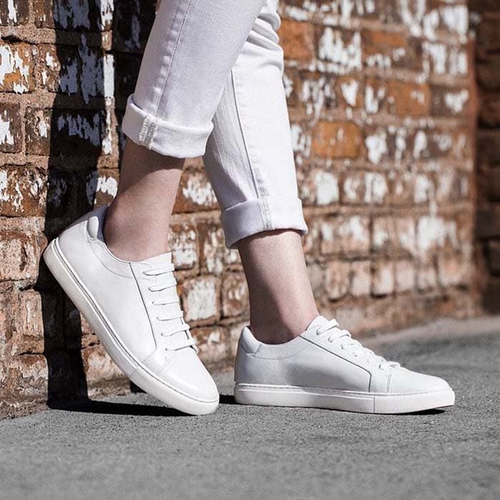 White Kenneth Cole “Kam” sneakers showcase the minimalist low-profile silhouette and clean leather finish that made the versatile style a celebrity favorite for off-duty dressing and airport travel